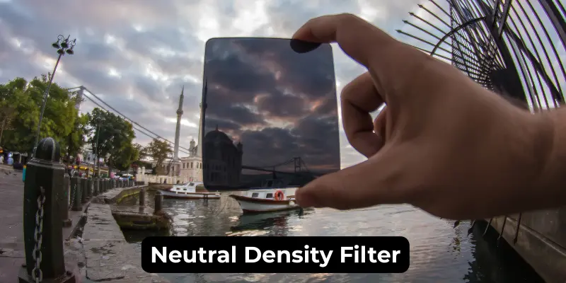 Neutral Density Filter Held In Hand In Front Of A Landscape, Reducing Light For Long Exposure Effects And Enhancing The Scene.